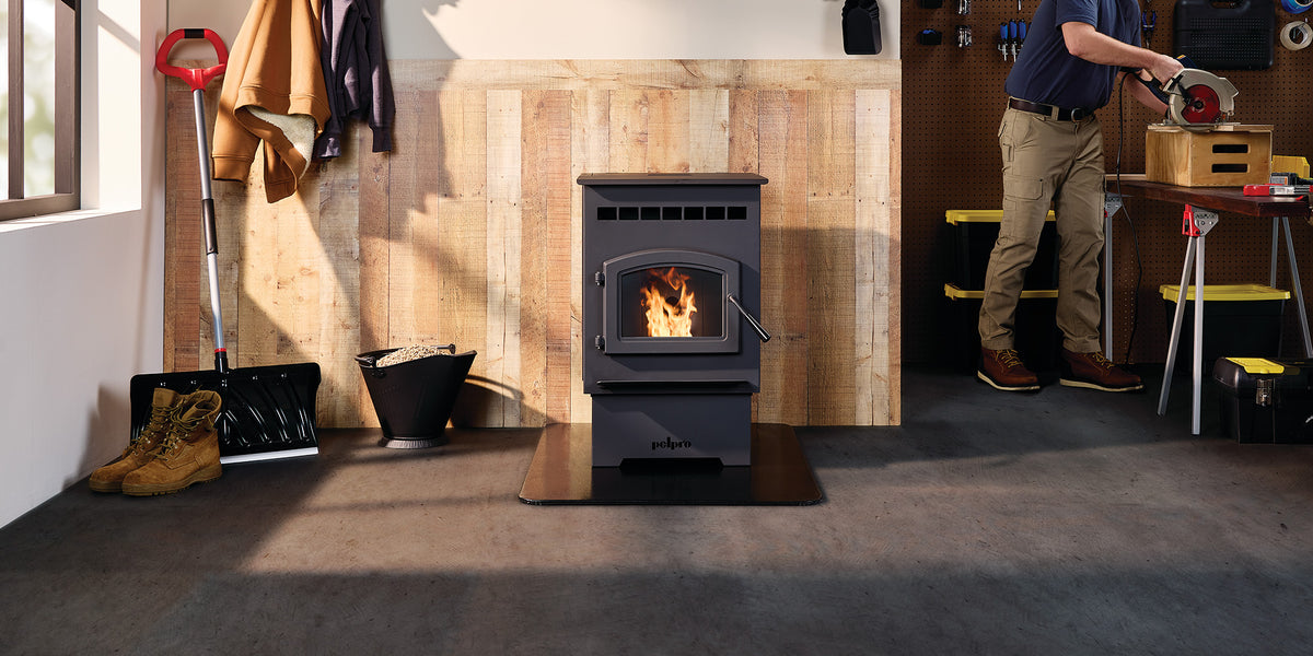 Pellet stove burning in a workshop; shovel, boots, and tools nearby. Person cutting wood on workbench.