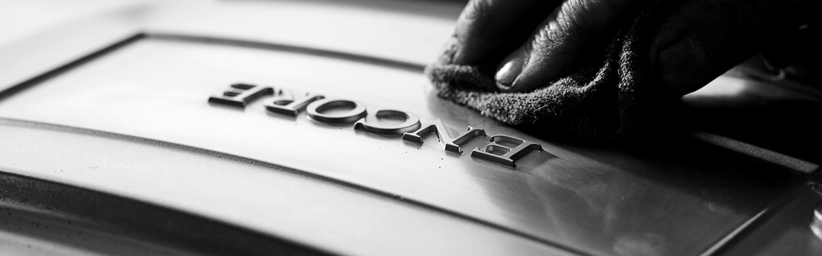 Hand polishing raised "ENCORE" letters on metal surface, with a cloth in a close-up, monochrome setting.