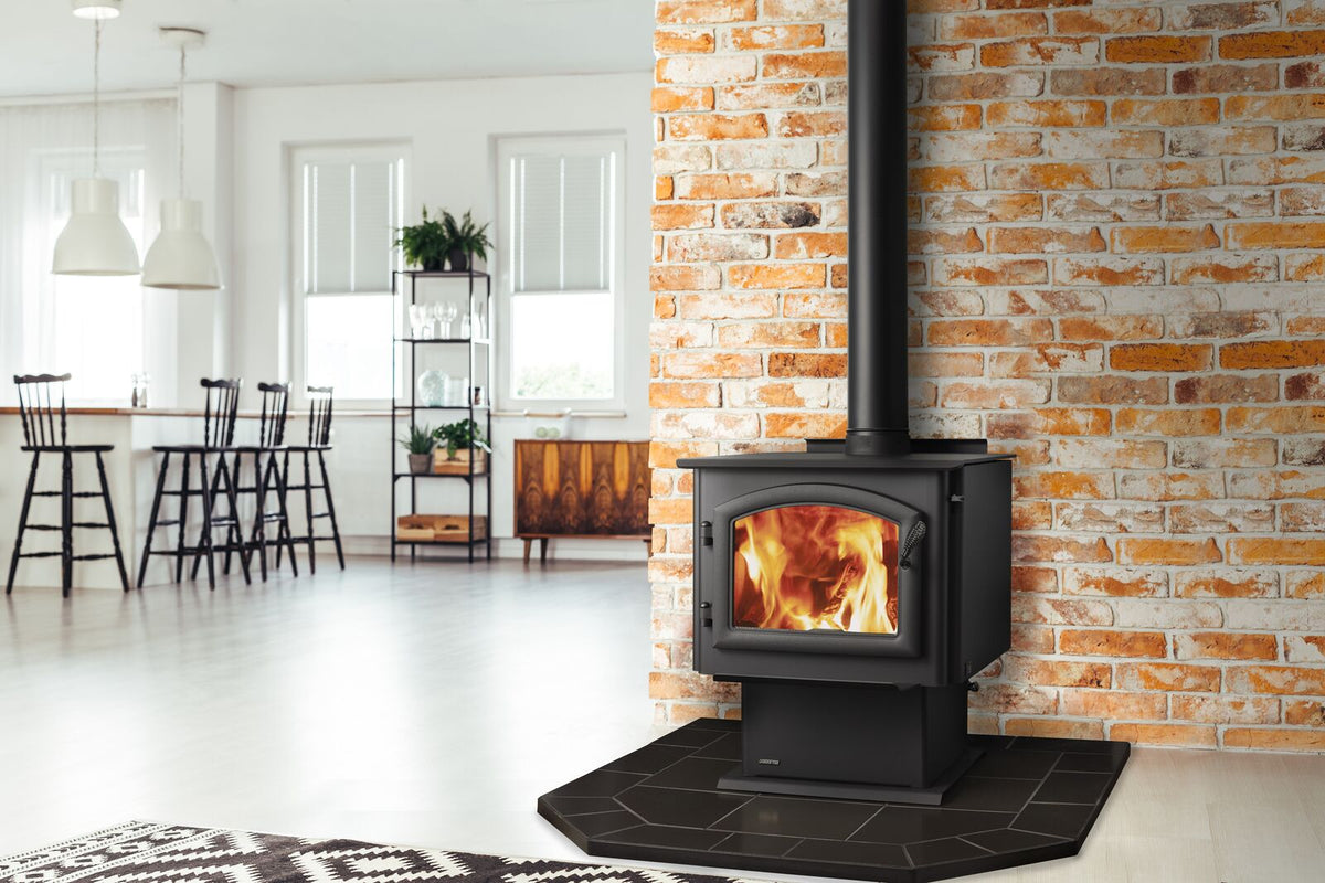 Wood stove burning in a cozy room, featuring white walls, brick accents, bar stools, and leafy plants.